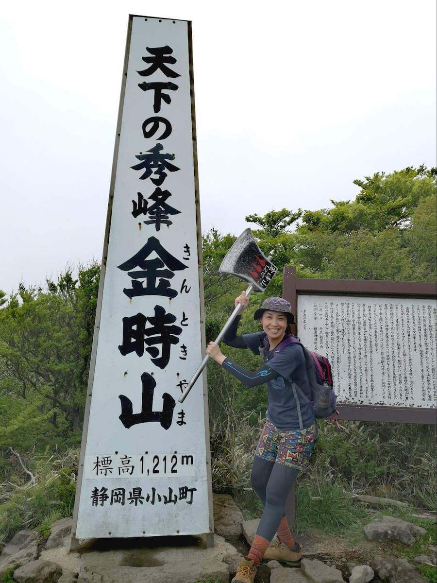 金時山の頂上にある「天下の秀峰 金時山」と書かれた看板をバックに「まさかり」を担いだ高島麻利央さんの写真